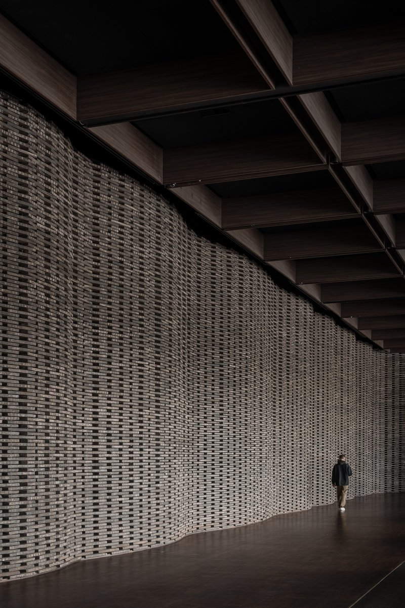 Long perforated brick screen wall with coffered timber ceiling and a lone figure walking