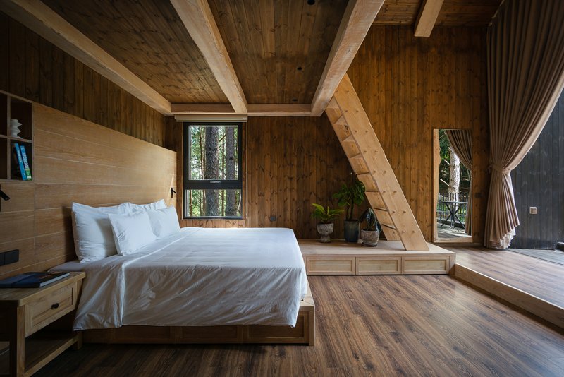 Bedroom interior with exposed timber beams, wood ladder, and windows framing forest views