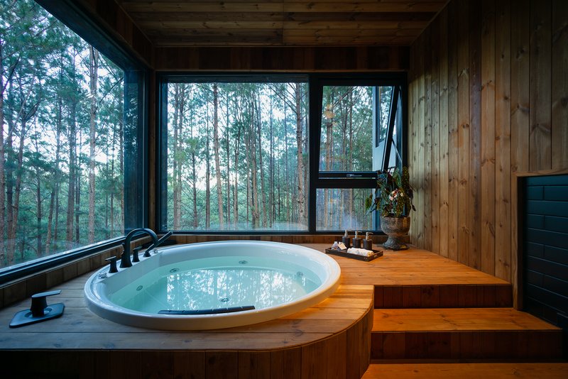 Sunken bathtub with timber surround and stepped platform overlooking misty forest through glazed walls