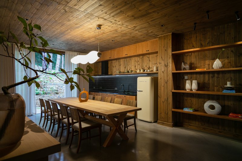 Dining room with vaulted timber ceiling and open shelving beside a glazed courtyard with greenery