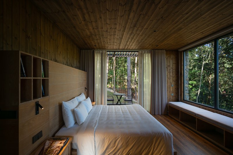 Bedroom with timber-clad ceiling and full-height glazing opening to a tree-filled courtyard beyond