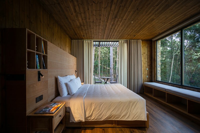 Bedroom opening to a glazed balcony with forest views through floor-to-ceiling windows and curtains