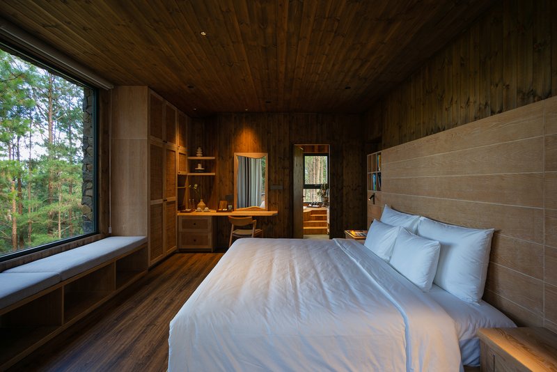 Timber-lined bedroom with corner window seat overlooking the surrounding pine forest at dusk