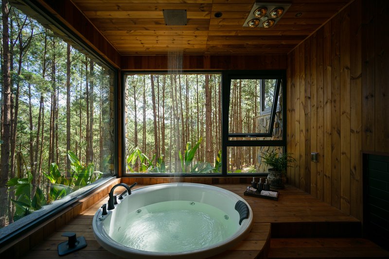 Circular jacuzzi set into timber deck framed by corner windows facing dense forest vegetation