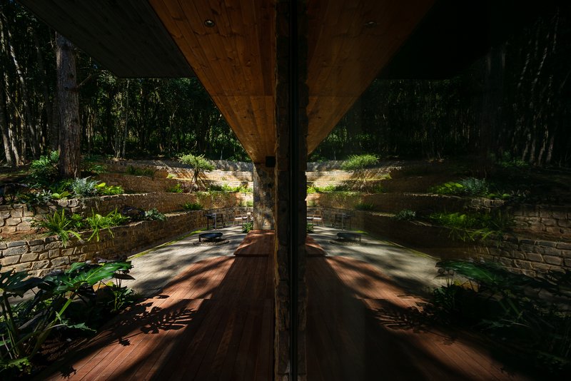 Corner column reflecting terraced garden beds and timber soffit in a glass wall surface