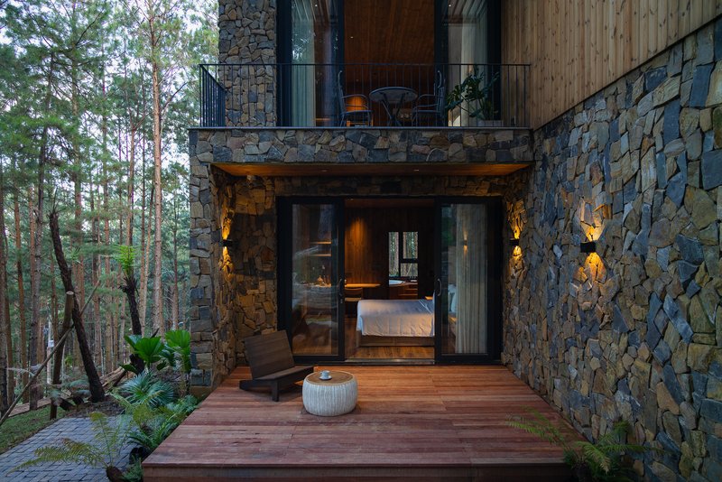 Timber deck terrace leading to glazed bedroom entry framed by stacked stone walls and forest