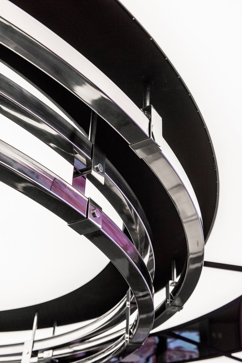 Close-up of curved black metal banding wrapping around purple glass panels in an interior stairwell