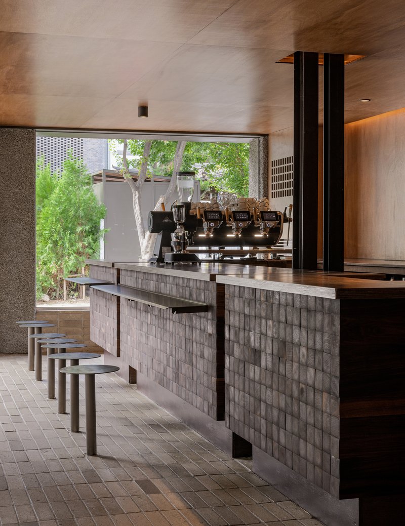 Coffee bar counter with ribbed tile cladding and espresso machine beneath timber ceiling