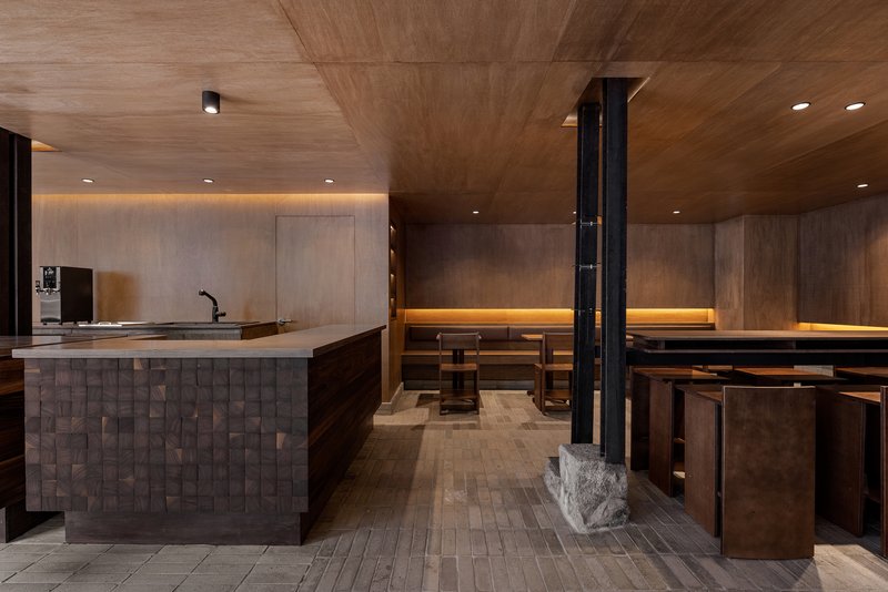 Interior of a tea room with textured wood ceiling, stone counter, and black steel columns with carved stone bases