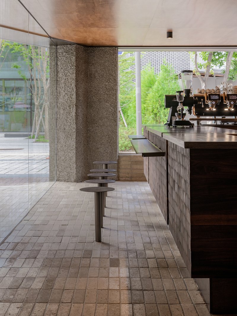 Rough stone wall beside a counter with circular metal stools overlooking a planted courtyard through large windows