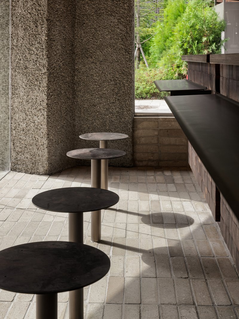 Close-up of four circular stools with metal stems aligned along a counter beneath textured stone walls