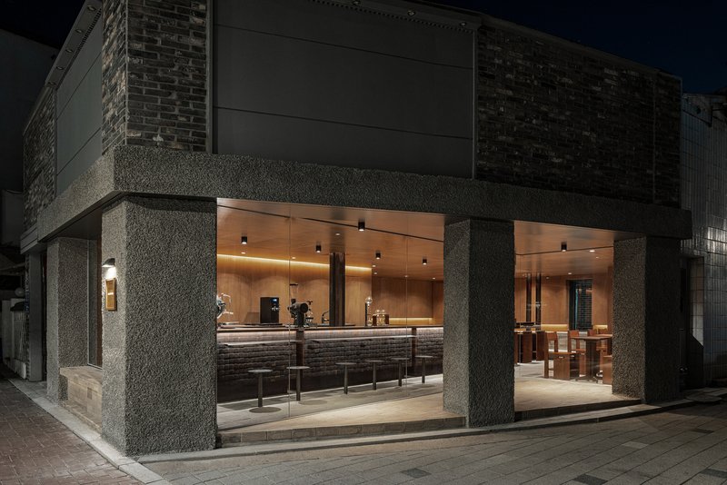 Street corner view of the open glass facade with textured concrete columns at night
