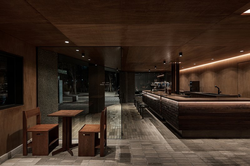 View through the entrance towards the long counter bar with dark tile base and wood seating