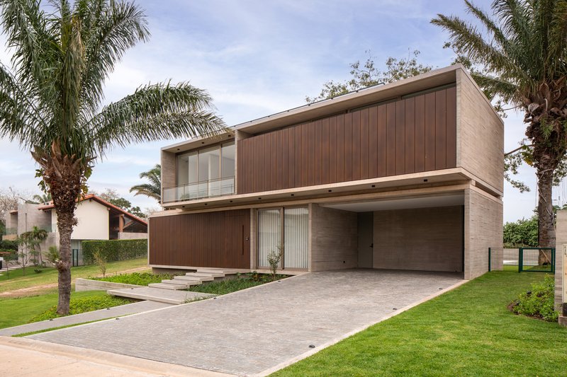 Two-story facade featuring timber-clad volumes above a recessed carport with palm trees flanking the driveway
