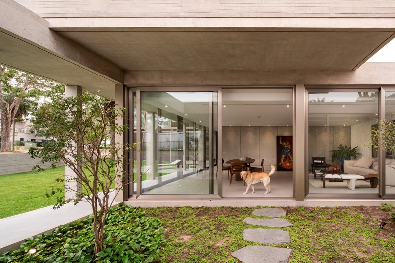 Covered outdoor space with concrete soffit, floor-to-ceiling glazing, dog inside, and planted courtyard garden