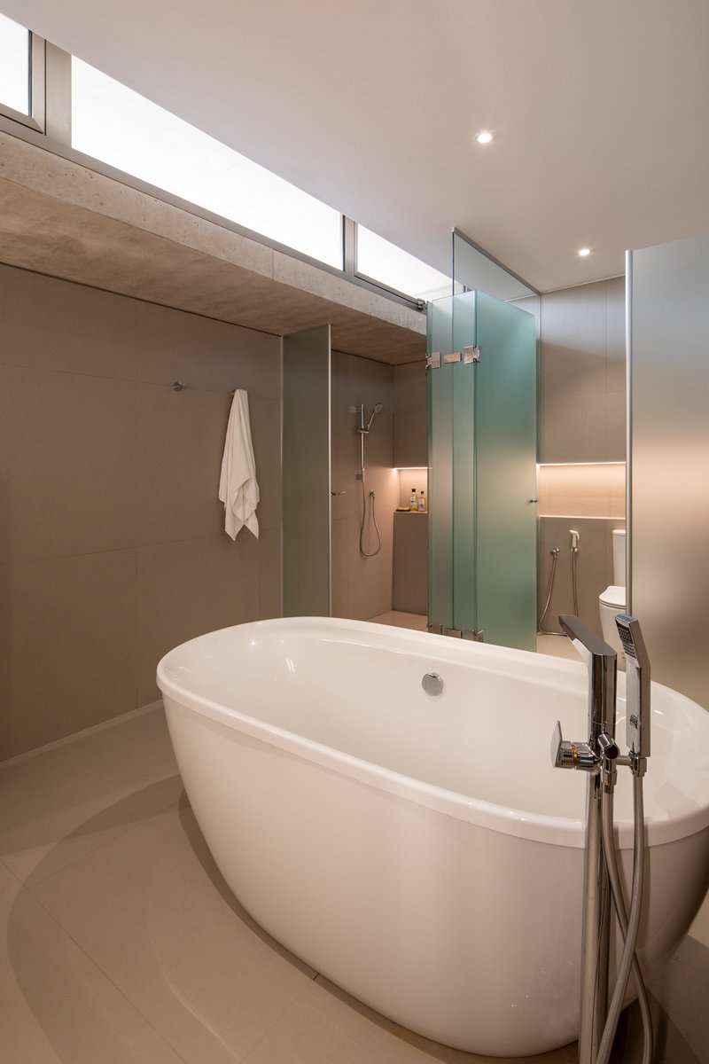 Freestanding bathtub beneath a horizontal clerestory window with frosted glass shower enclosure beyond