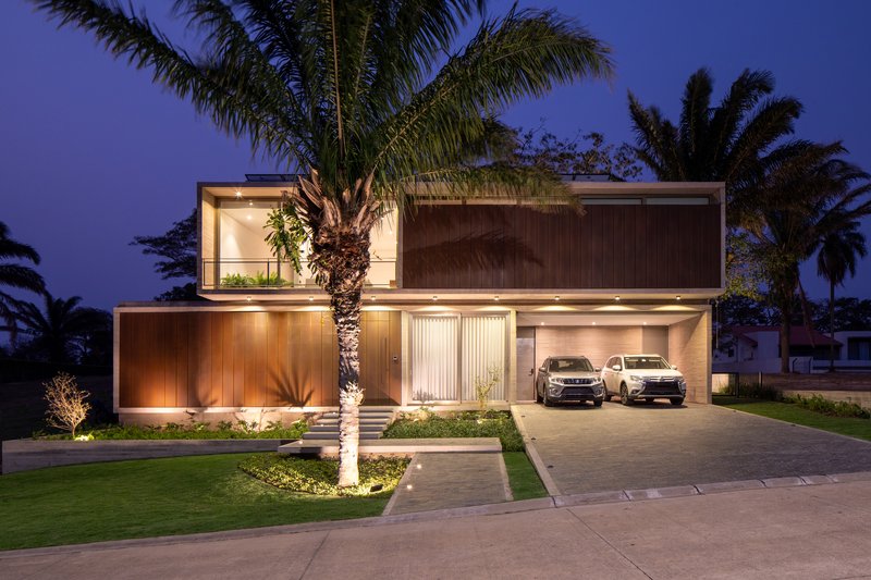 Front elevation showing garage, entry, and timber-clad volumes framed by palm trees at night