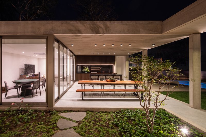 Covered dining terrace with concrete frame opening to planted courtyard and pool at night