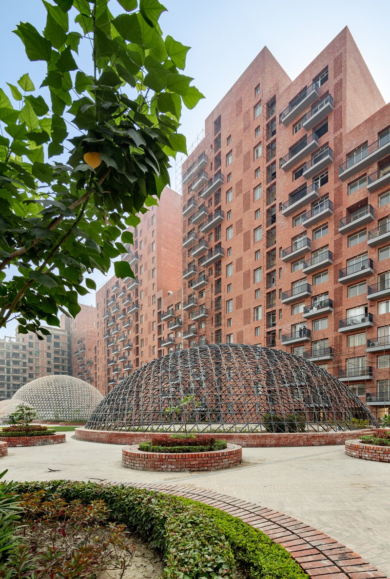 Steel geodesic dome in a courtyard plaza with residential towers and green foliage in the foreground