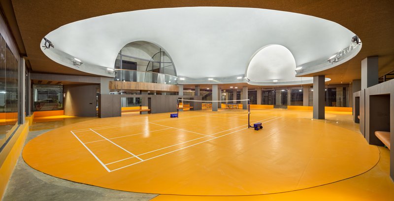 Indoor sports court with bright orange flooring beneath a circular white ceiling with skylights