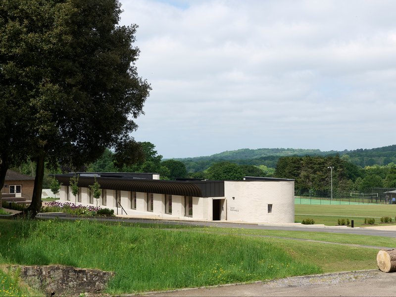 Low-rise pavilion with corrugated barrel-vault roof and pale brick walls set beside a sports field