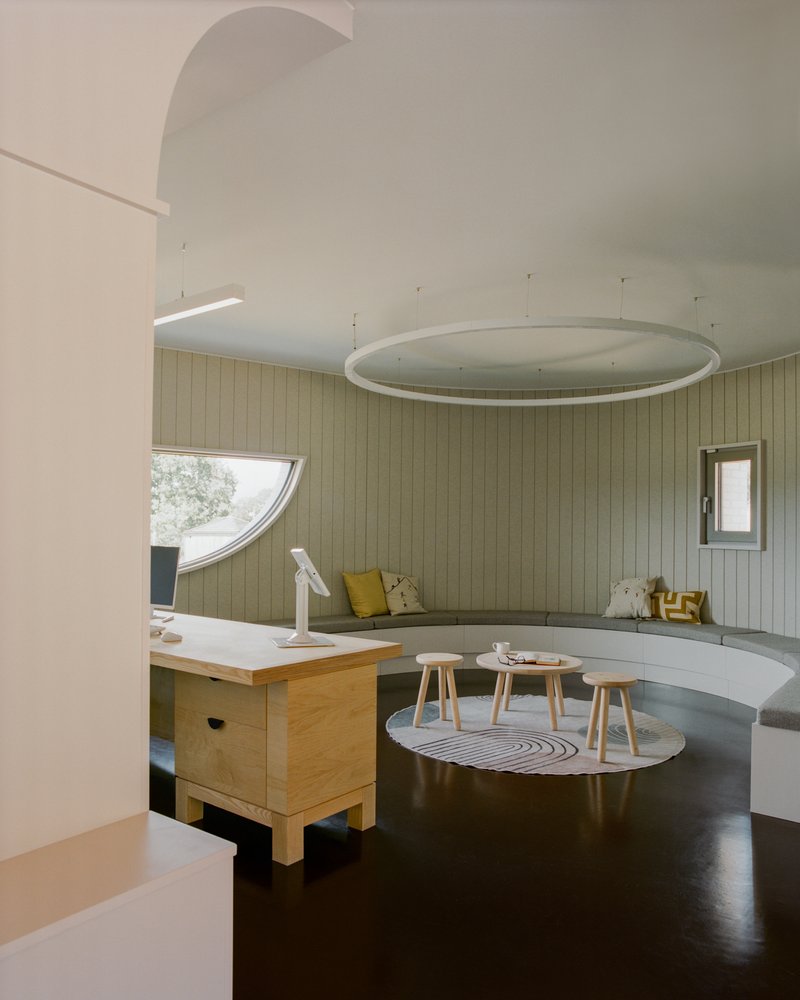 Interior with curved benches against pale timber walls and circular light fixture suspended from vaulted ceiling