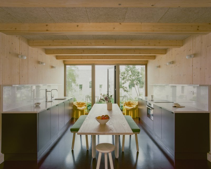 Kitchen with timber ceiling beams and central dining table looking toward glazed doors and planted courtyard