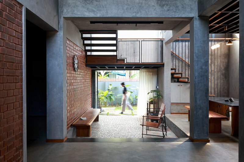 Entry hall with concrete columns and mezzanine bridge framing view to garden with figure walking