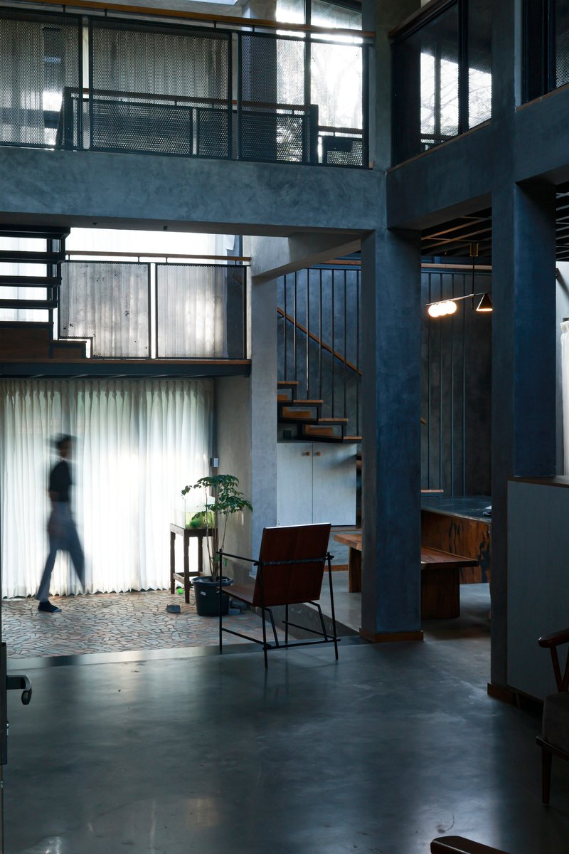 Double-height living space with steel staircase and mezzanine bridges lit by filtered daylight
