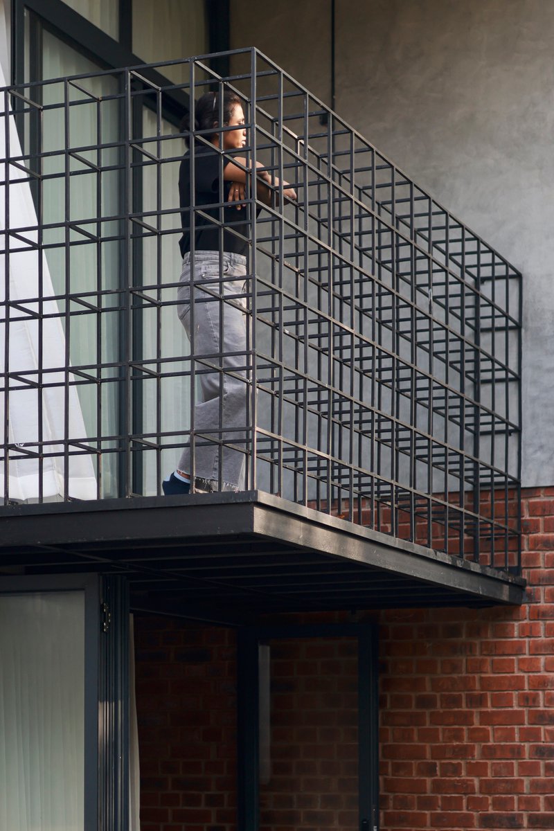 Steel grid staircase with person ascending between concrete slab and brick wall