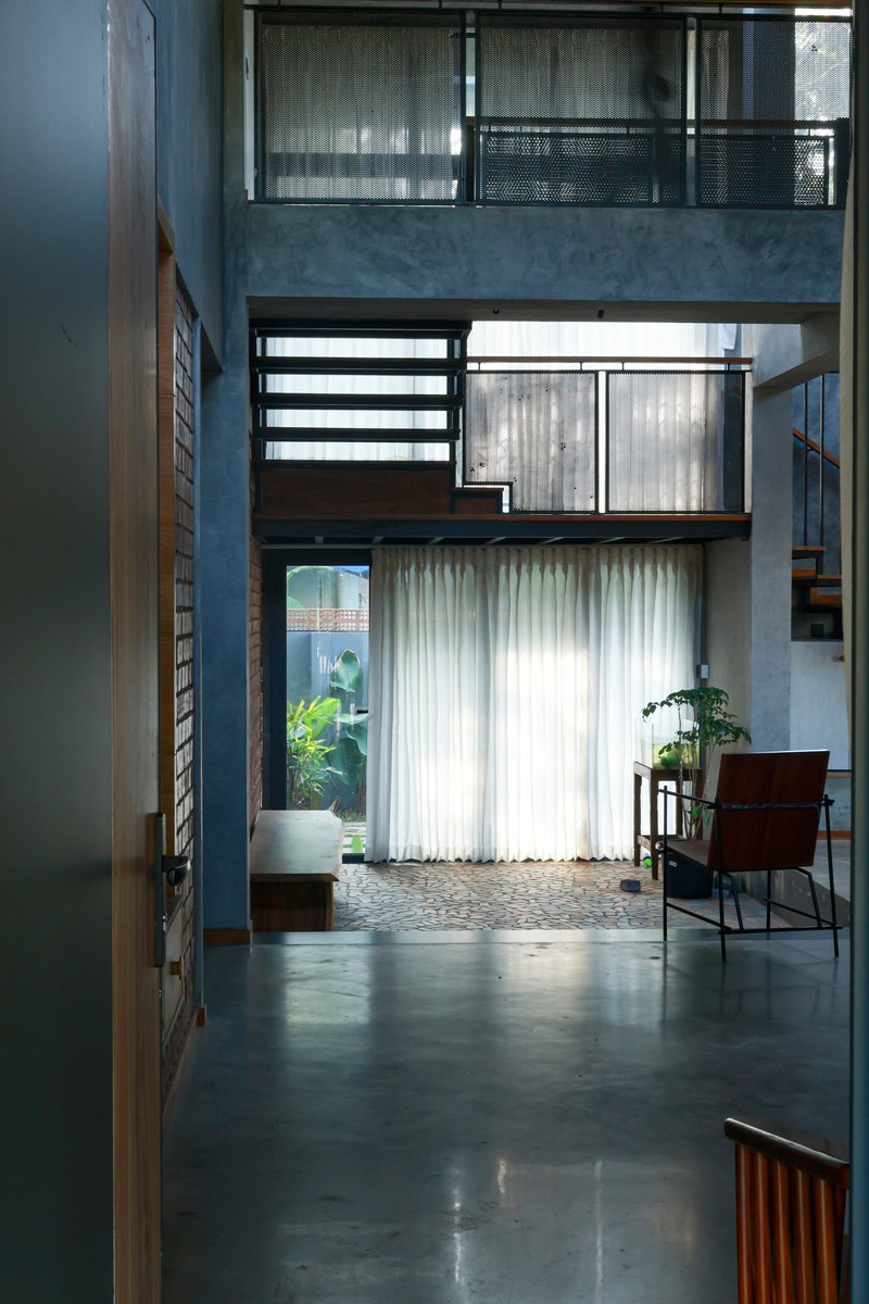 Three-level interior void with stacked balconies, concrete walls, and sheer curtains over polished concrete floors