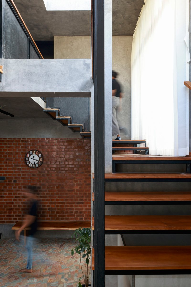 Timber and steel staircase bridging exposed brick wall and concrete landing with figures in motion below
