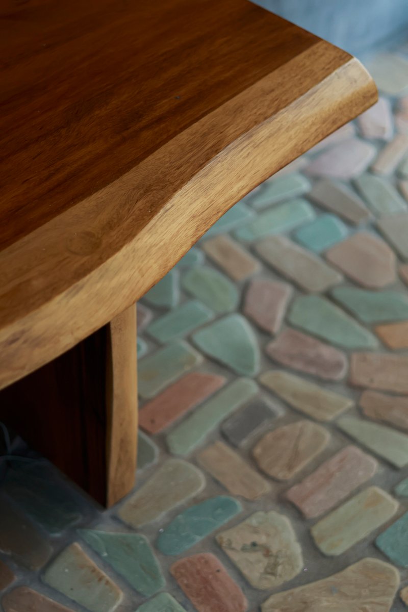 Close-up of rounded timber table edge above patterned pebble floor in pastel tones