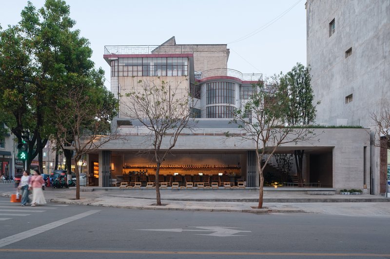 Illuminated cafe interior visible from the street at dusk with pedestrians crossing in the foreground
