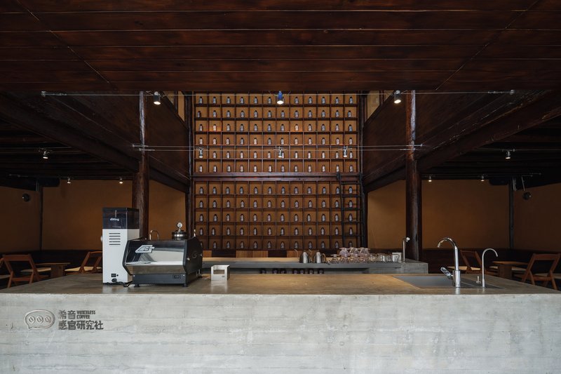 Service counter with espresso machine facing a gridded wooden storage wall beneath dark timber ceiling planks