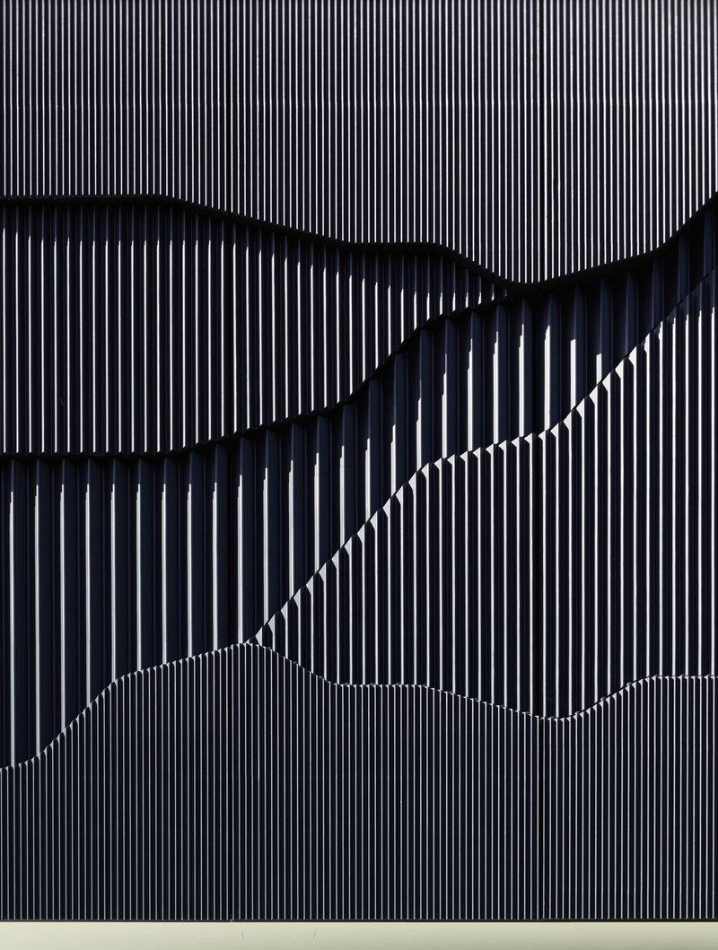 Close-up of vertical metal fin cladding forming wave-like shadows across the facade surface