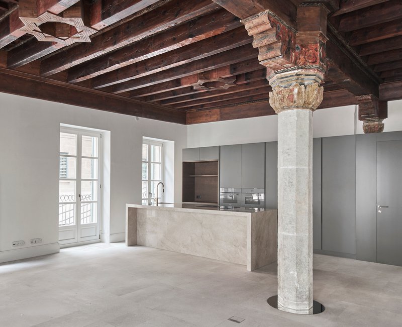 Open kitchen with marble island and grey cabinetry beneath exposed timber beams and an ornamental stone column