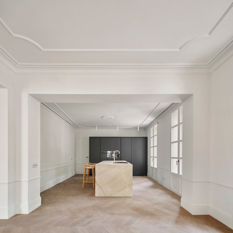 Kitchen with stone island and dark cabinetry framed by white paneled walls and glazed doors