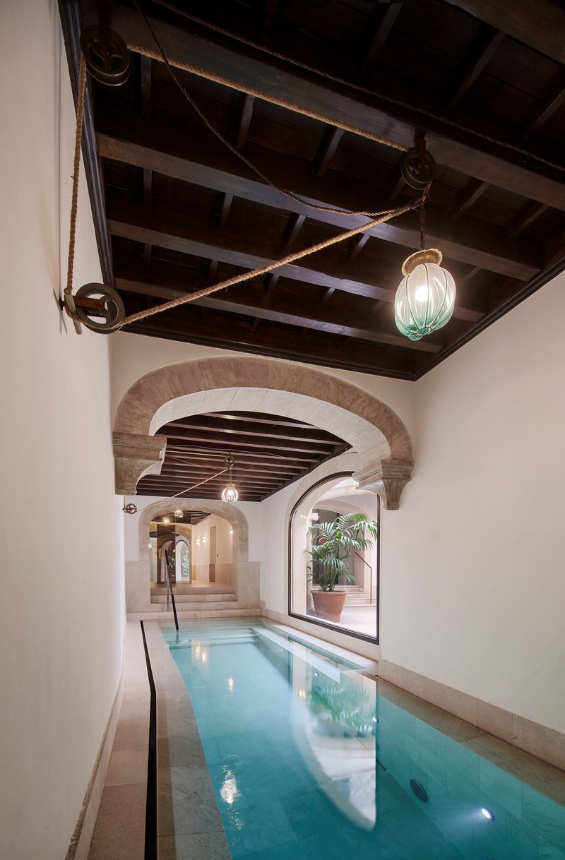 Interior lap pool corridor with stone arches, dark timber ceiling, and hanging glass pendant light
