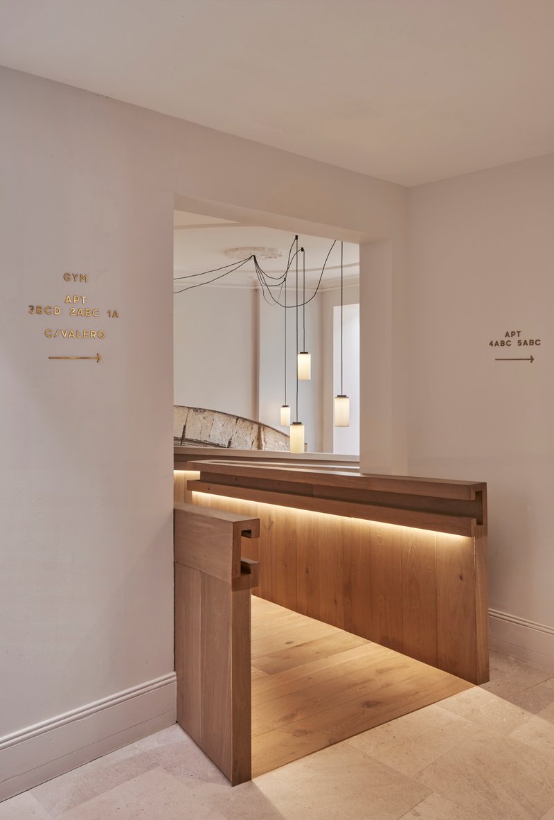 Reception desk of timber with integrated lighting below multi-drop pendant lights and directional signage