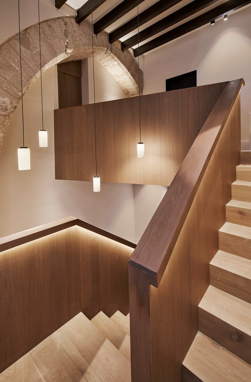 Stairwell with walnut handrail and pendant lights beneath a restored stone arch and timber ceiling beams