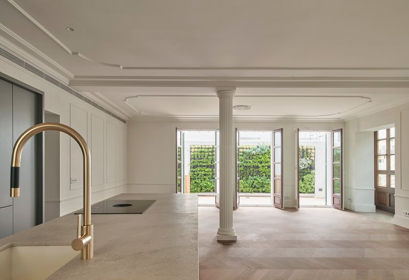 Kitchen island with brass faucet facing fluted column and tall windows opening to greenery outside