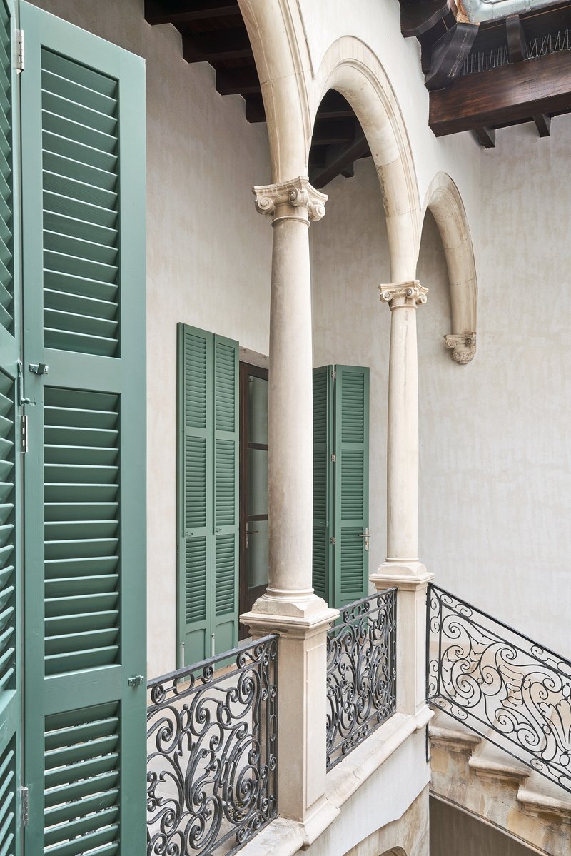 Upper-level courtyard with green louvered shutters, white stucco walls, ornamental iron railings and exposed timber beams