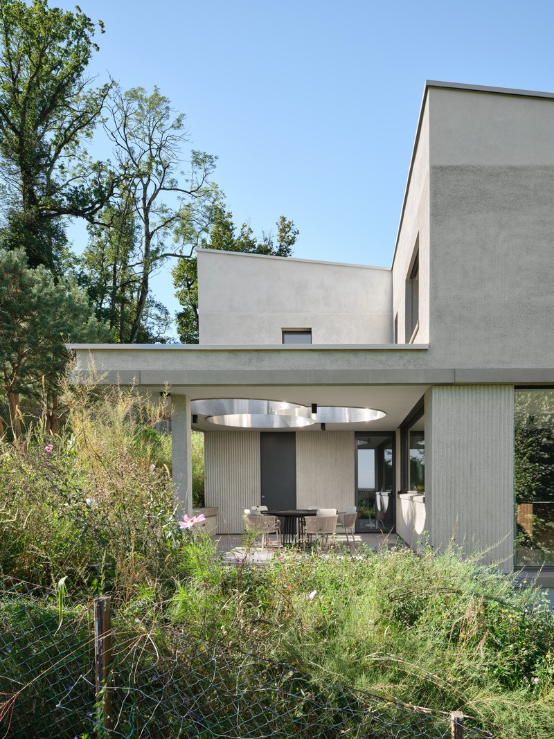 Covered outdoor terrace with concrete frame and circular skylight opening above a dining area in daylight