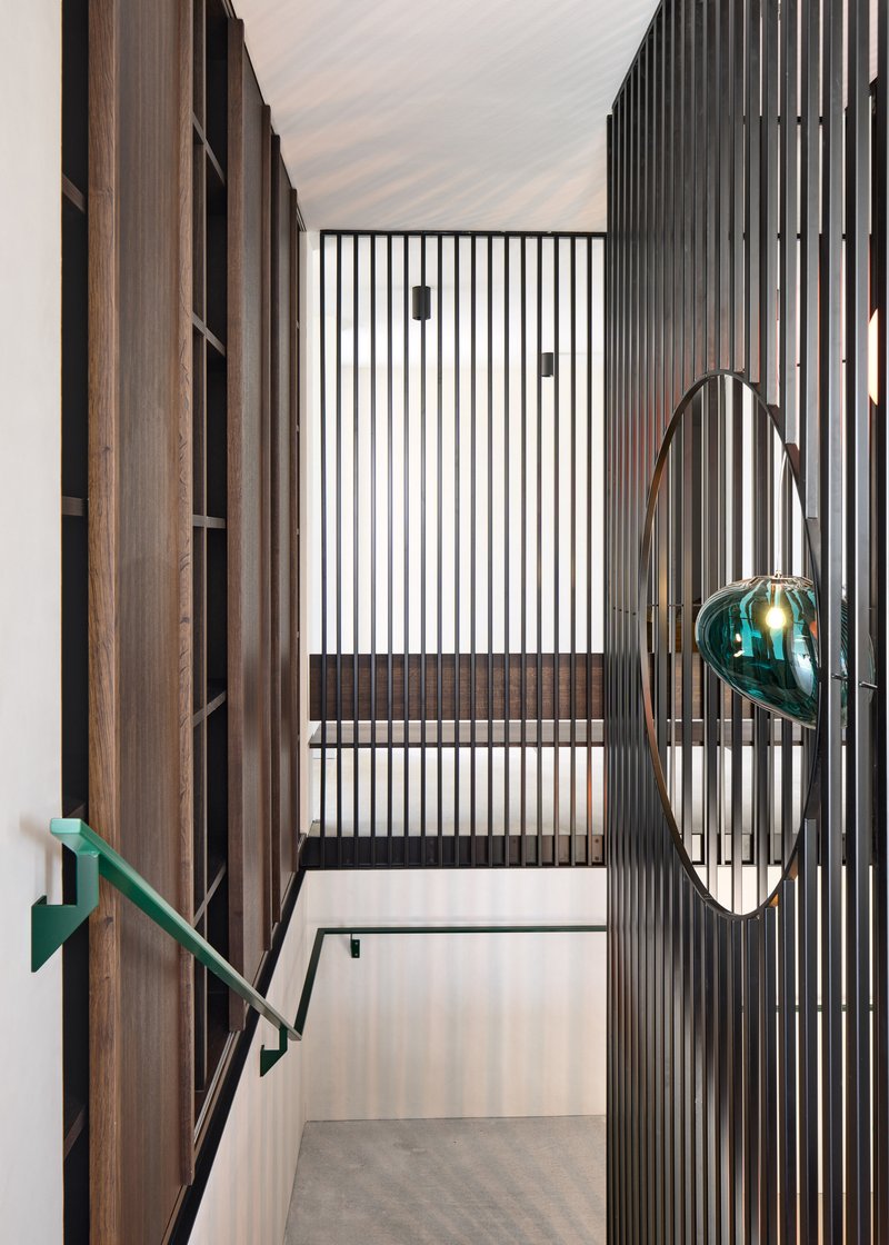 Stairway landing with vertical timber slats and suspended green glass light fixture in daylight