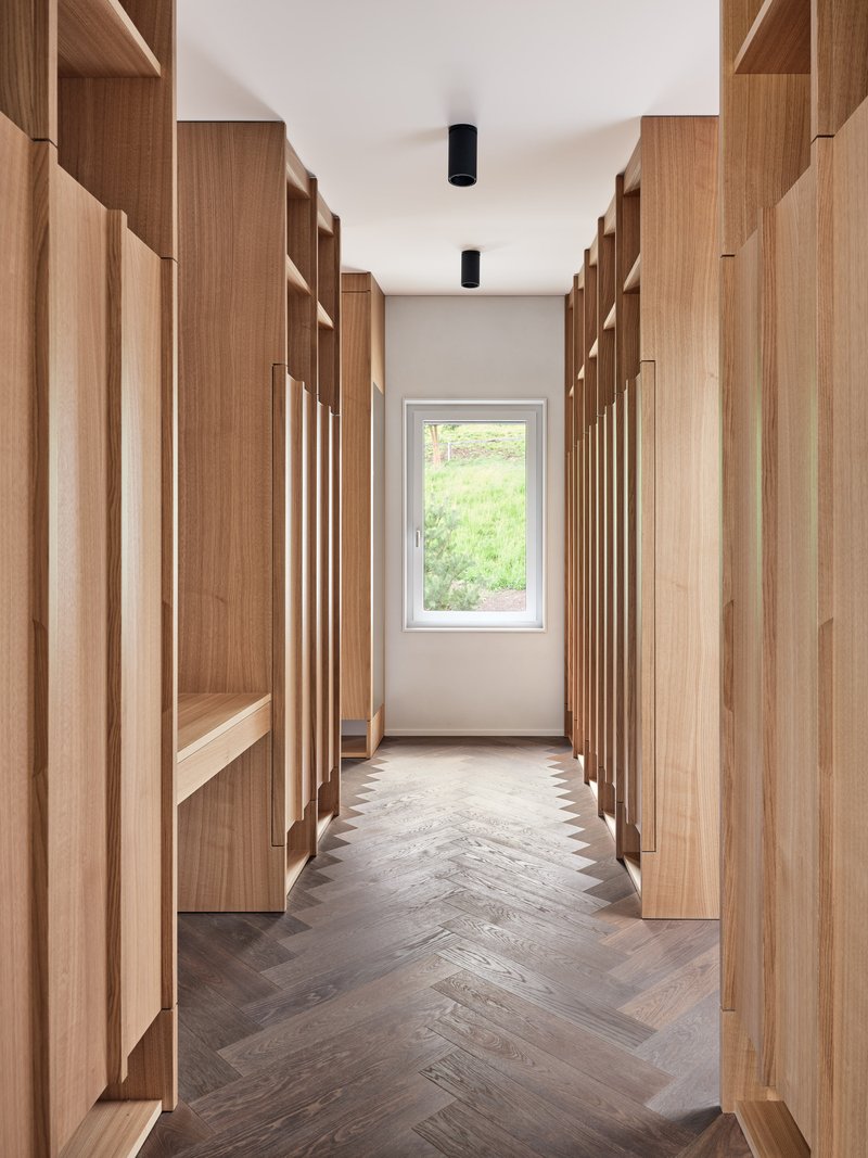 Corridor with chevron wood flooring flanked by timber shelving leading to window with garden view