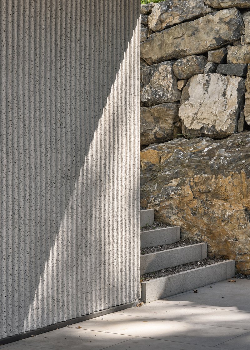 Detail of ribbed concrete wall meeting stone outcrop with concrete steps in dappled sunlight