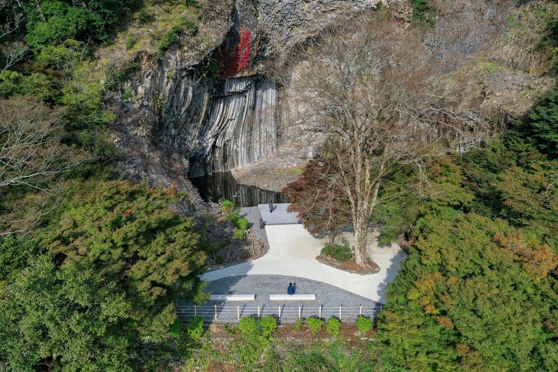 Concrete observation deck wrapping around preserved trees at the base of the striated rock formation