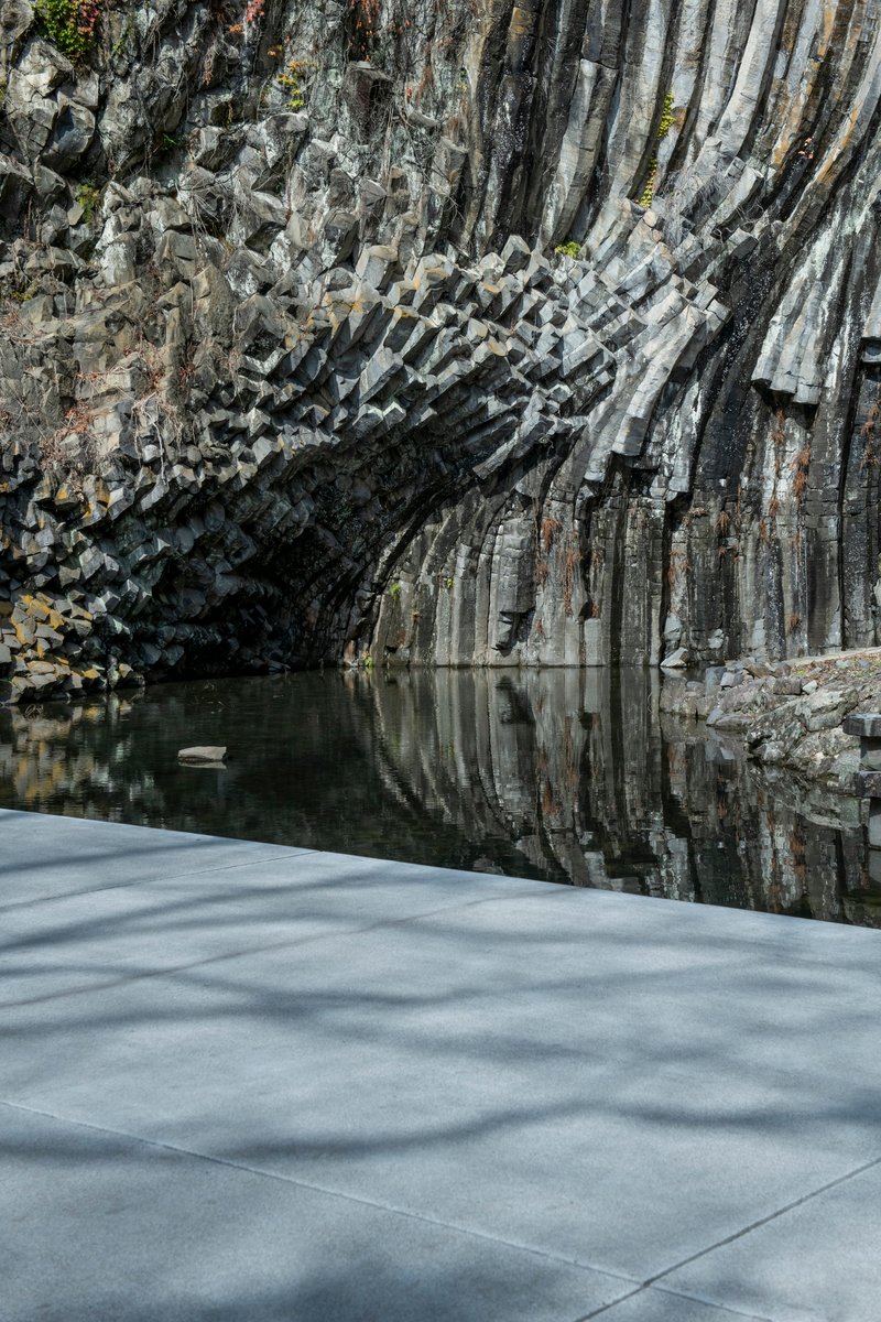 Concrete roof edge meeting the fractured basalt cliff face above a reflecting pool