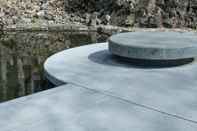 Layered circular concrete platforms beside a reflecting pool with quarried rock wall beyond